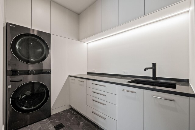 washroom with dark tile patterned flooring, sink, stacked washer and dryer, and cabinets