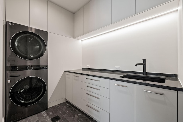 laundry room featuring a sink, cabinet space, stacked washer and dryer, and marble finish floor