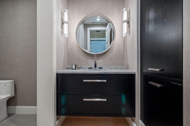 bathroom featuring toilet, wood finished floors, wallpapered walls, baseboards, and vanity