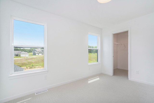 unfurnished bedroom featuring a walk in closet, multiple windows, a closet, and carpet floors