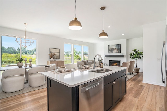 kitchen featuring sink, hanging light fixtures, light hardwood / wood-style floors, stainless steel dishwasher, and a center island with sink