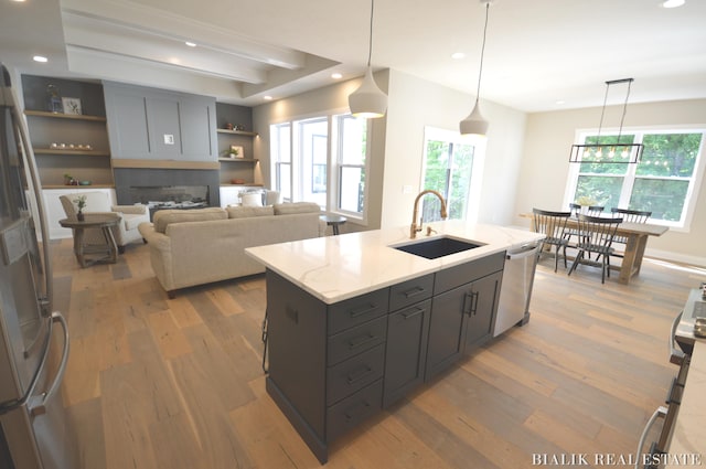 kitchen with light stone countertops, hanging light fixtures, light hardwood / wood-style floors, and sink