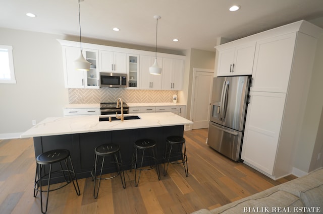 kitchen with stainless steel appliances, light wood-type flooring, white cabinetry, and a kitchen bar