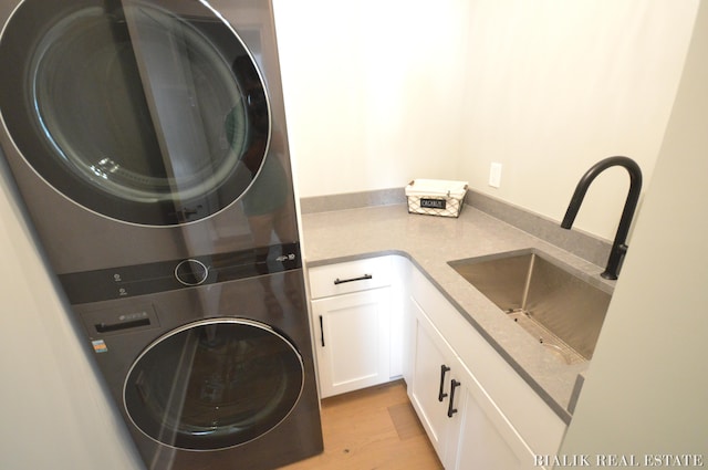 laundry area with sink, cabinets, light wood-type flooring, and stacked washer / drying machine