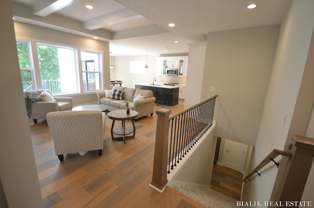 living room featuring wood-type flooring, sink, and beamed ceiling