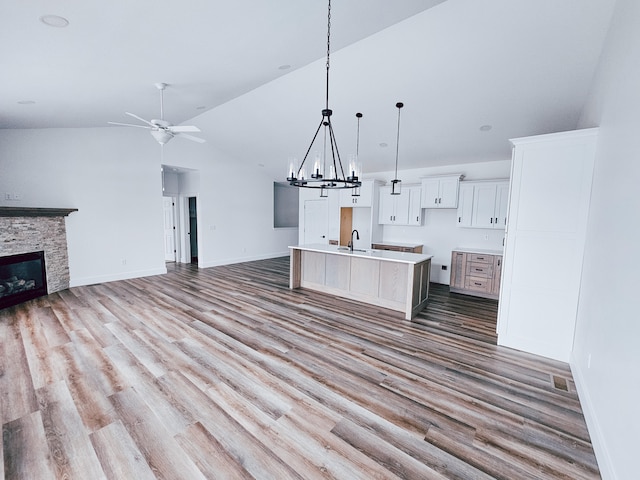 interior space with ceiling fan with notable chandelier, a stone fireplace, an island with sink, and light hardwood / wood-style floors