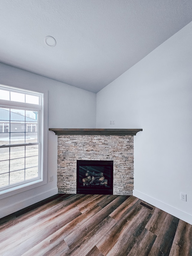 unfurnished living room with wood-type flooring, a stone fireplace, and a wealth of natural light