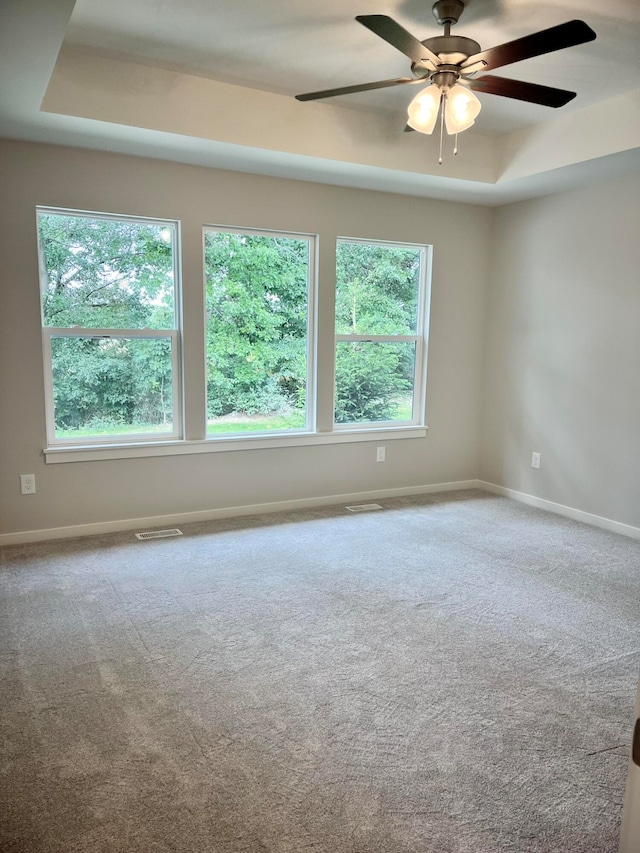 carpeted empty room with a raised ceiling and ceiling fan