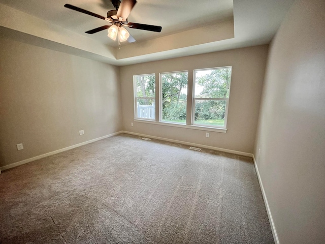 carpeted spare room featuring ceiling fan and a raised ceiling