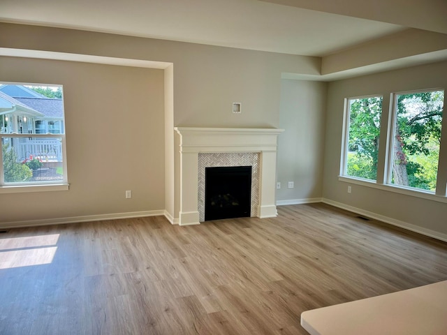 unfurnished living room featuring light hardwood / wood-style floors, a tile fireplace, and a wealth of natural light