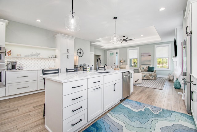 kitchen featuring ceiling fan, an island with sink, a raised ceiling, stainless steel appliances, and light hardwood / wood-style flooring