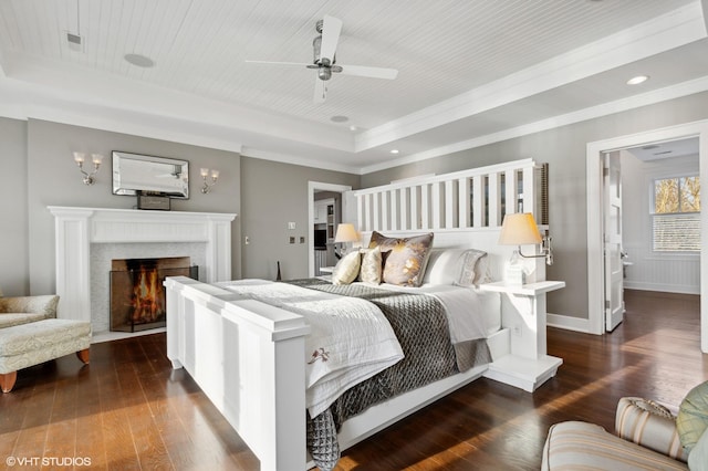 bedroom with dark hardwood / wood-style flooring, a tray ceiling, a premium fireplace, and ceiling fan