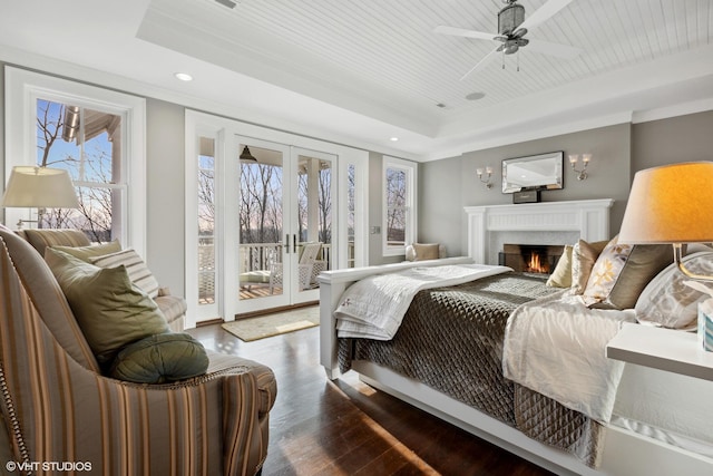 bedroom with ceiling fan, access to outside, a tray ceiling, hardwood / wood-style floors, and french doors