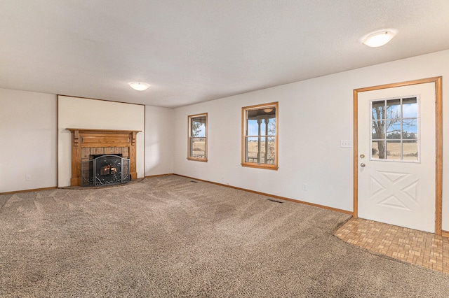 unfurnished living room featuring a wealth of natural light, a textured ceiling, carpet floors, and a fireplace