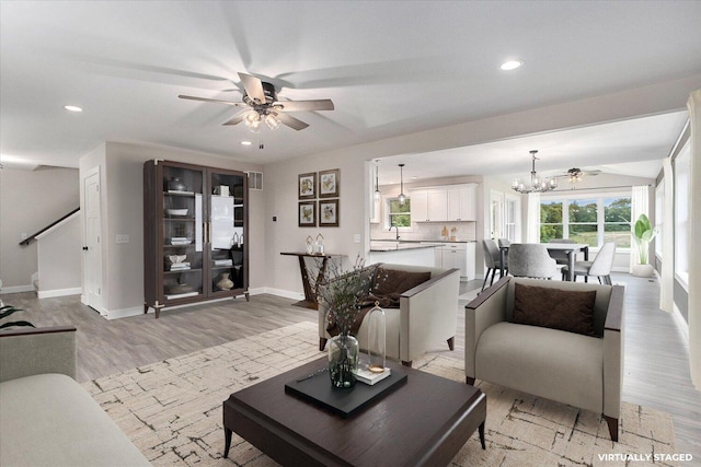 living room with sink, ceiling fan with notable chandelier, and light hardwood / wood-style flooring