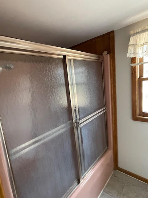 bathroom with combined bath / shower with glass door and tile flooring