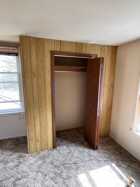 unfurnished bedroom featuring a closet, light carpet, and wooden walls