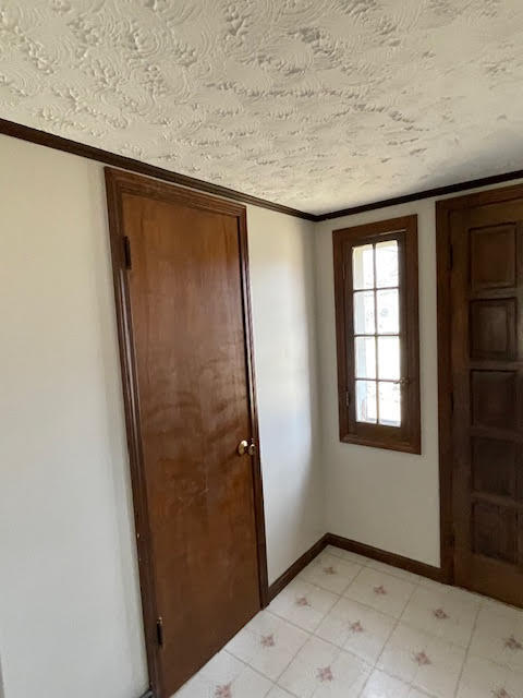 entrance foyer featuring a textured ceiling, ornamental molding, and light tile floors