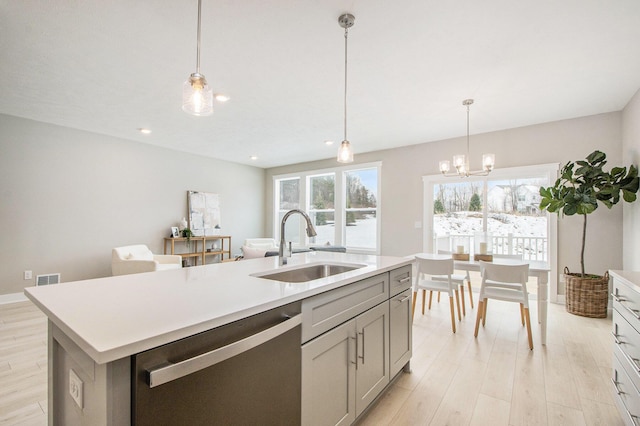 kitchen featuring decorative light fixtures, sink, stainless steel dishwasher, a center island with sink, and light hardwood / wood-style flooring