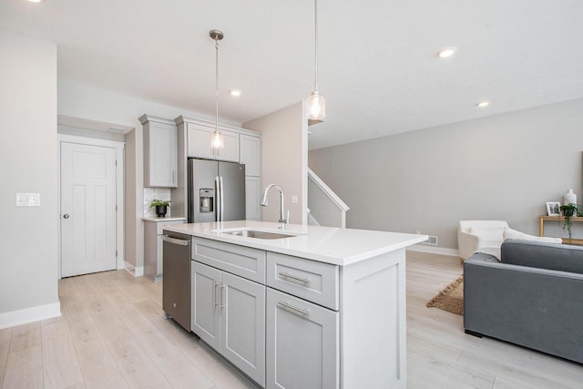 kitchen featuring sink, appliances with stainless steel finishes, gray cabinetry, a center island with sink, and decorative light fixtures