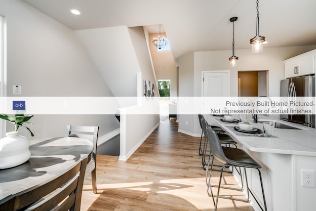 kitchen with pendant lighting, white cabinets, stainless steel fridge, light stone countertops, and light wood-type flooring