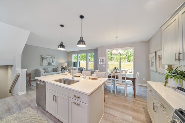 kitchen with a center island with sink, appliances with stainless steel finishes, decorative light fixtures, sink, and light hardwood / wood-style flooring