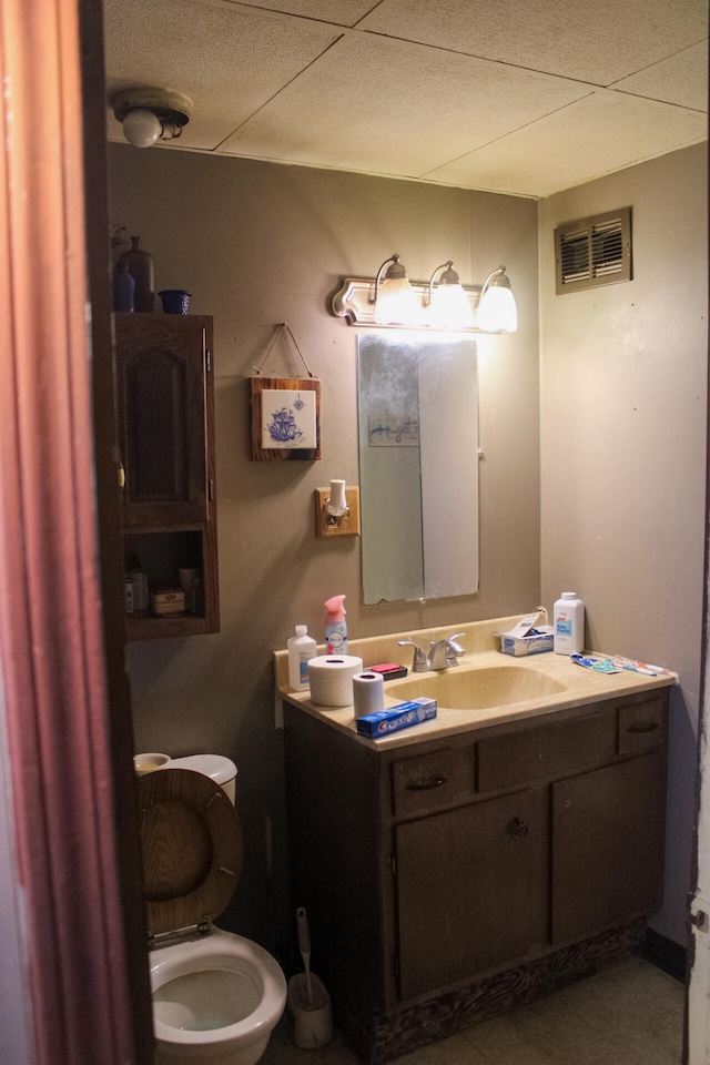 bathroom featuring toilet, vanity, and a drop ceiling