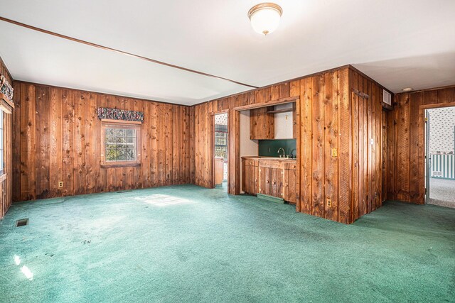 unfurnished living room featuring sink, wooden walls, and carpet floors