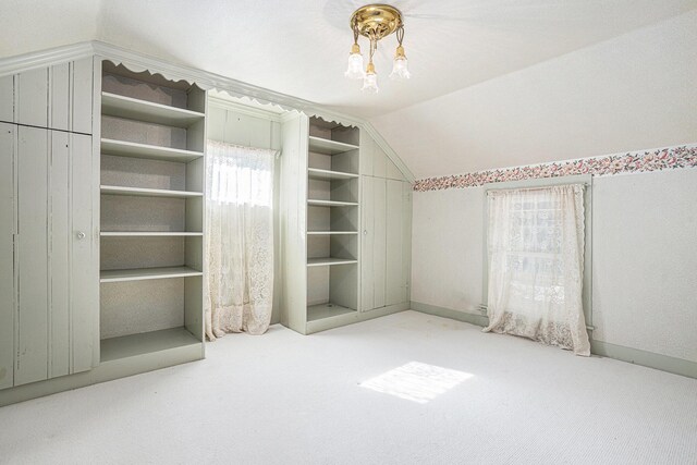 additional living space featuring built in shelves, light carpet, and vaulted ceiling