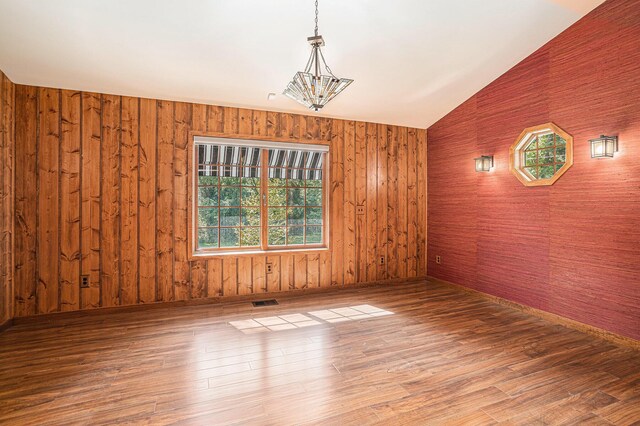 empty room featuring wood walls, vaulted ceiling, and hardwood / wood-style flooring