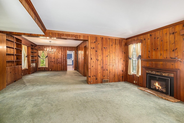 unfurnished living room with wooden walls, ornamental molding, light colored carpet, and an inviting chandelier