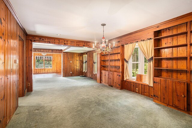 carpeted empty room with a notable chandelier and wood walls