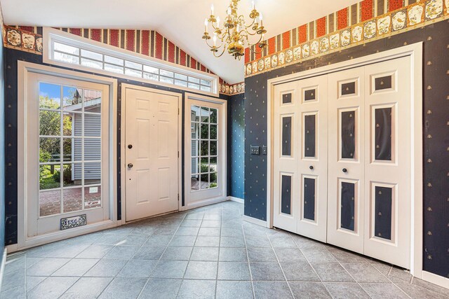 doorway with a notable chandelier, light tile patterned flooring, vaulted ceiling, and a wealth of natural light