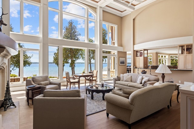 living room with a water view, a towering ceiling, coffered ceiling, and hardwood / wood-style floors