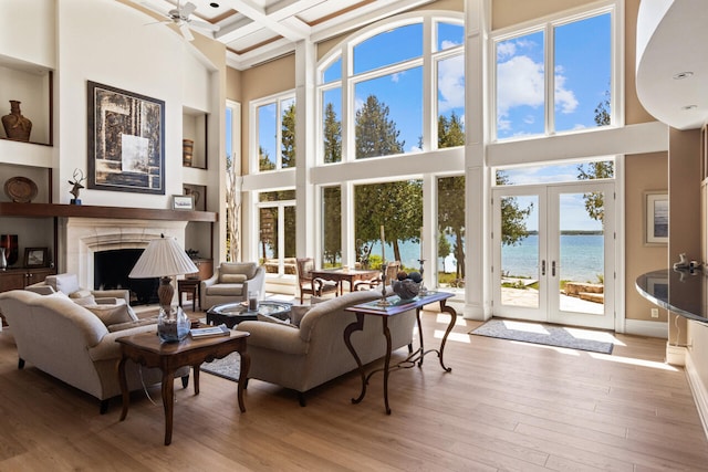 living room featuring a towering ceiling, a water view, coffered ceiling, light hardwood / wood-style floors, and beamed ceiling