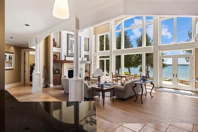 living room featuring decorative columns, a water view, light hardwood / wood-style floors, ornamental molding, and french doors