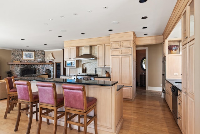 kitchen featuring a kitchen breakfast bar, tasteful backsplash, a fireplace, wall chimney exhaust hood, and light wood-type flooring