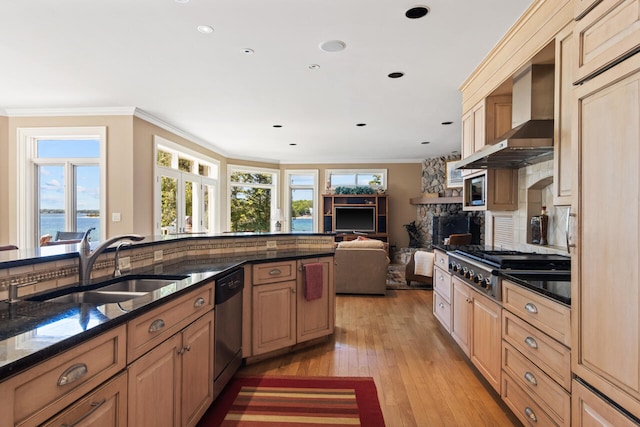 kitchen featuring sink, appliances with stainless steel finishes, dark stone countertops, a water view, and wall chimney exhaust hood