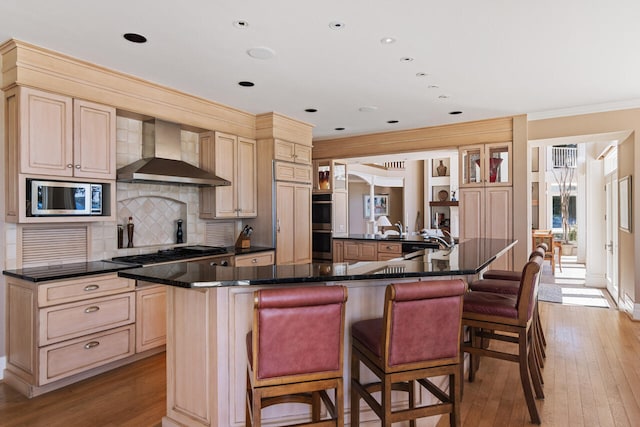 kitchen featuring a breakfast bar area, built in appliances, a large island, decorative backsplash, and wall chimney range hood