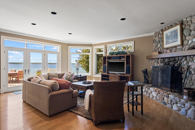 living room featuring crown molding, a water view, light hardwood / wood-style floors, a stone fireplace, and french doors