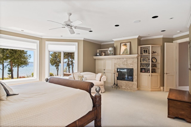 carpeted bedroom featuring a water view, ceiling fan, a premium fireplace, and crown molding