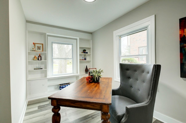 home office with light wood-type flooring and built in shelves