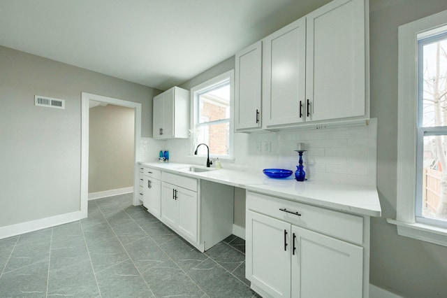 kitchen with backsplash, dark tile floors, a wealth of natural light, and white cabinets