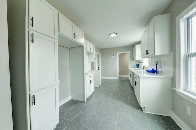 kitchen with backsplash, sink, dark tile floors, and white cabinetry