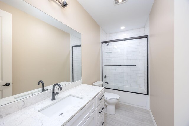 full bathroom featuring bath / shower combo with glass door, vanity, and toilet