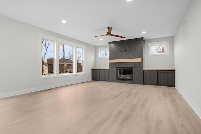 unfurnished living room with ceiling fan, a large fireplace, light hardwood / wood-style floors, and plenty of natural light