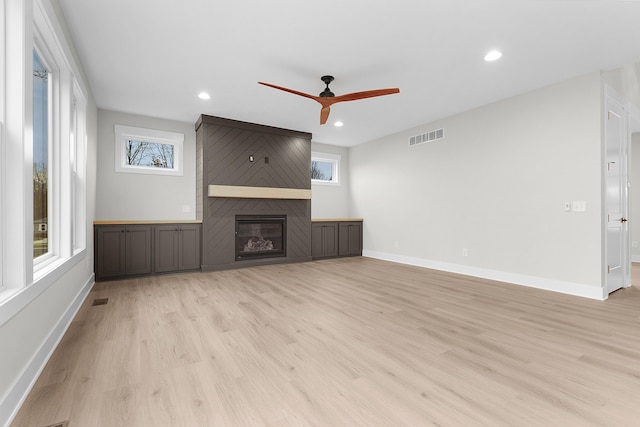 unfurnished living room featuring light wood-type flooring, a large fireplace, and ceiling fan