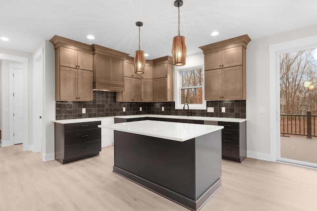 kitchen featuring light wood-type flooring, tasteful backsplash, sink, pendant lighting, and a kitchen island