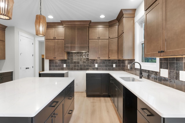 kitchen with sink, wall chimney range hood, pendant lighting, a kitchen island, and light wood-type flooring