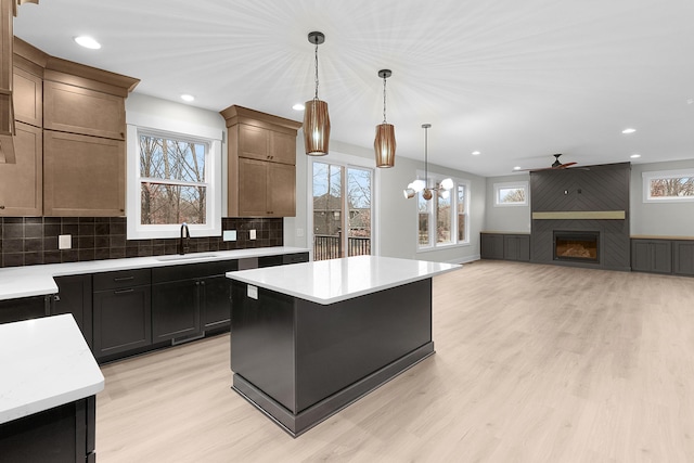 kitchen with a large fireplace, a center island, sink, backsplash, and ceiling fan with notable chandelier